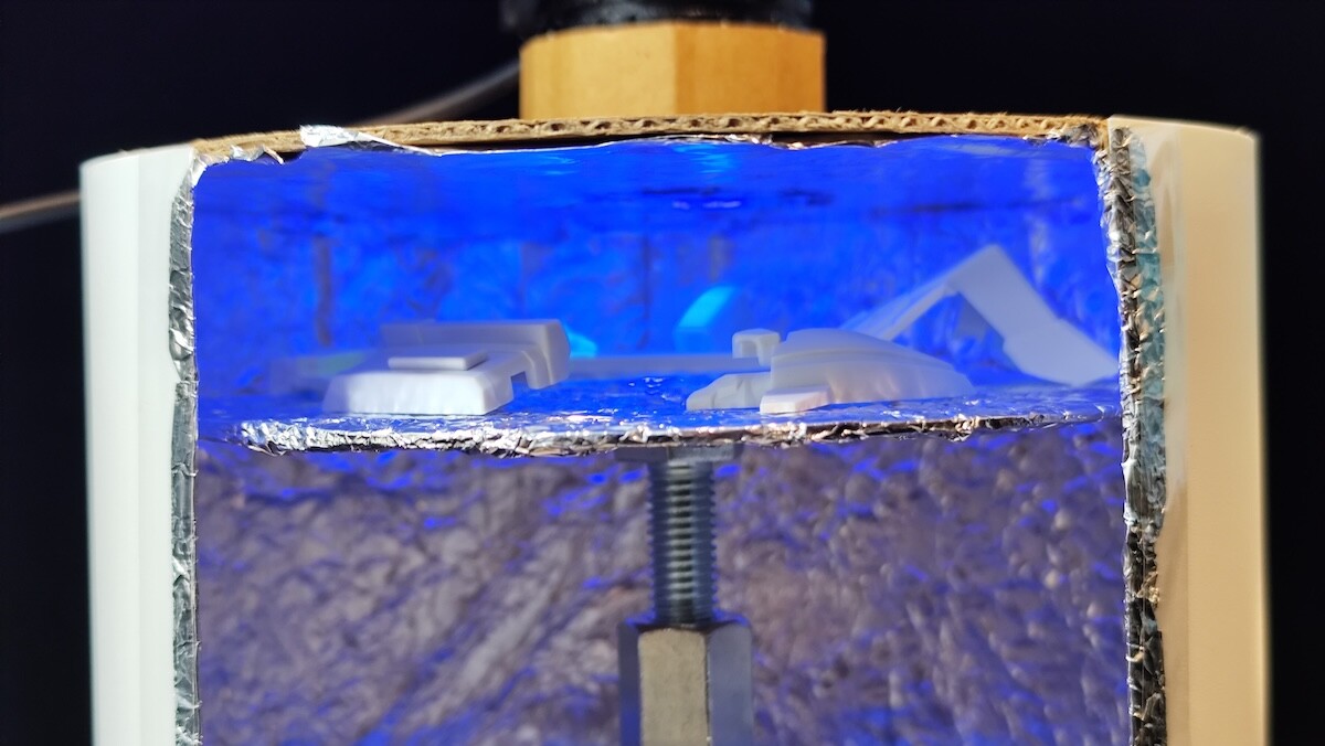 UV照射中のプラモデル用UV硬化促進ボックス内部。反射面とターンテーブルでパーツに光を当てている様子